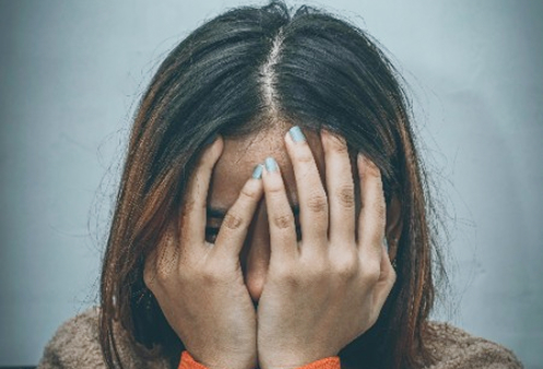 Uma mulher expressando tristeza, com os olhos fechados e as mãos cobrindo o rosto, representando a falta de energia e desânimo característicos da depressão.